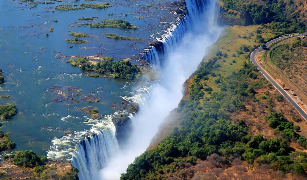 A breathtaking aerial view of Victoria Falls, Zimbabwe & Zambia, showcasing the majestic waterfall surrounded by lush greenery.