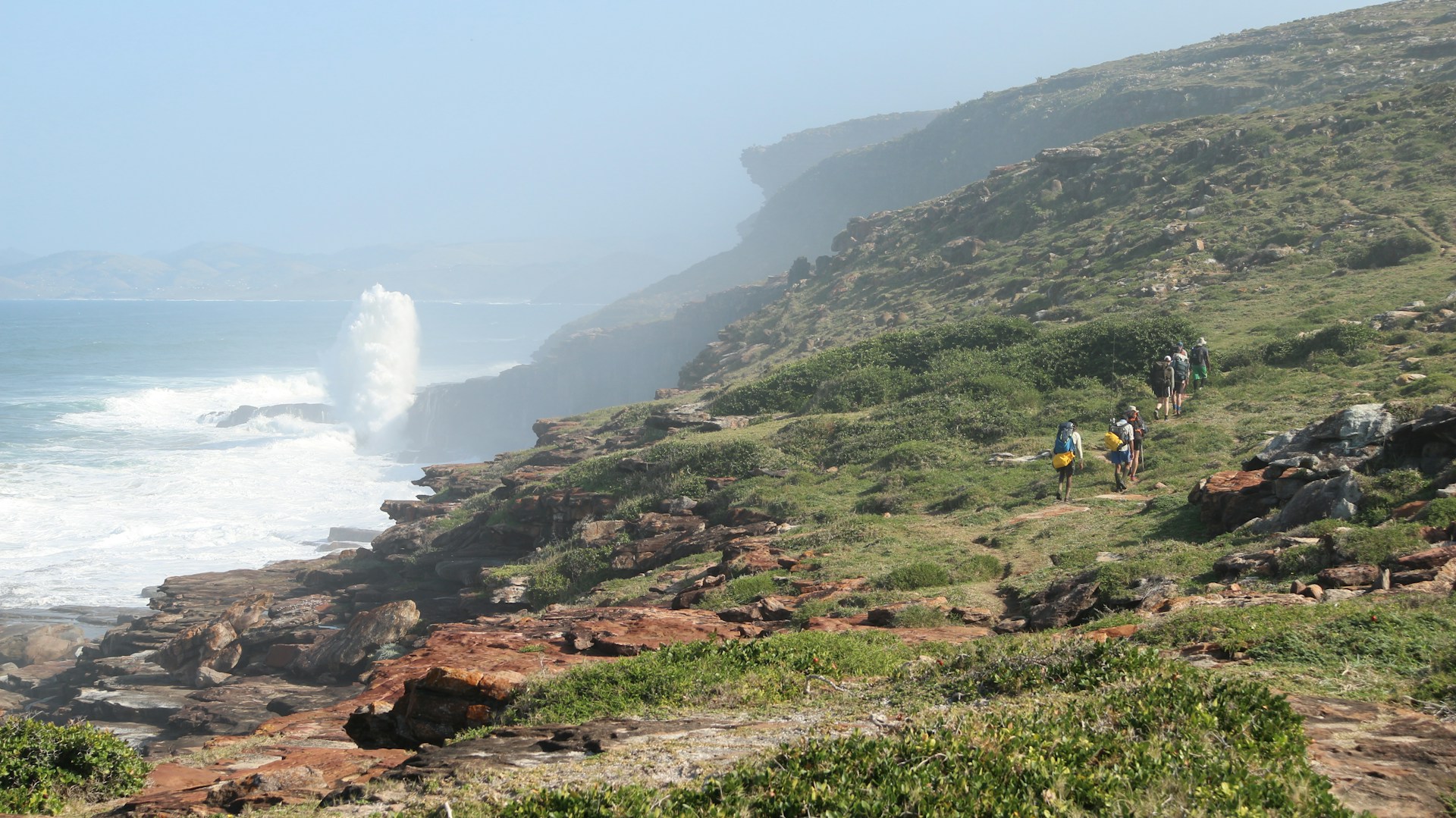 Eastern Cape: Scenic view of hikers trekking through the rugged Eastern Cape mountains, with the sparkling sea visible in the background, showcasing the natural beauty of South Africa.