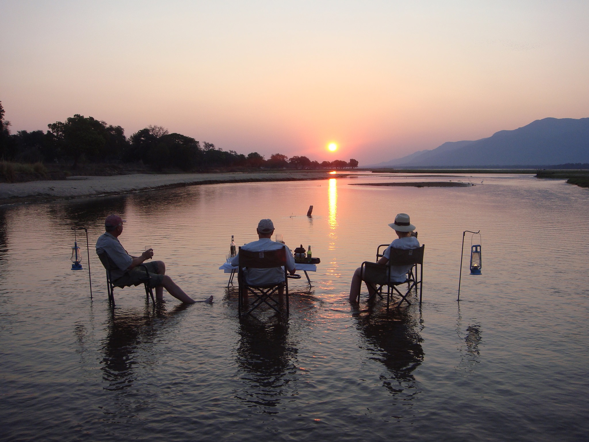 Mana Pools National Park, Zimbabwe: John Camp with three elderly people enjoying beers while sitting in chairs surrounded by nature.