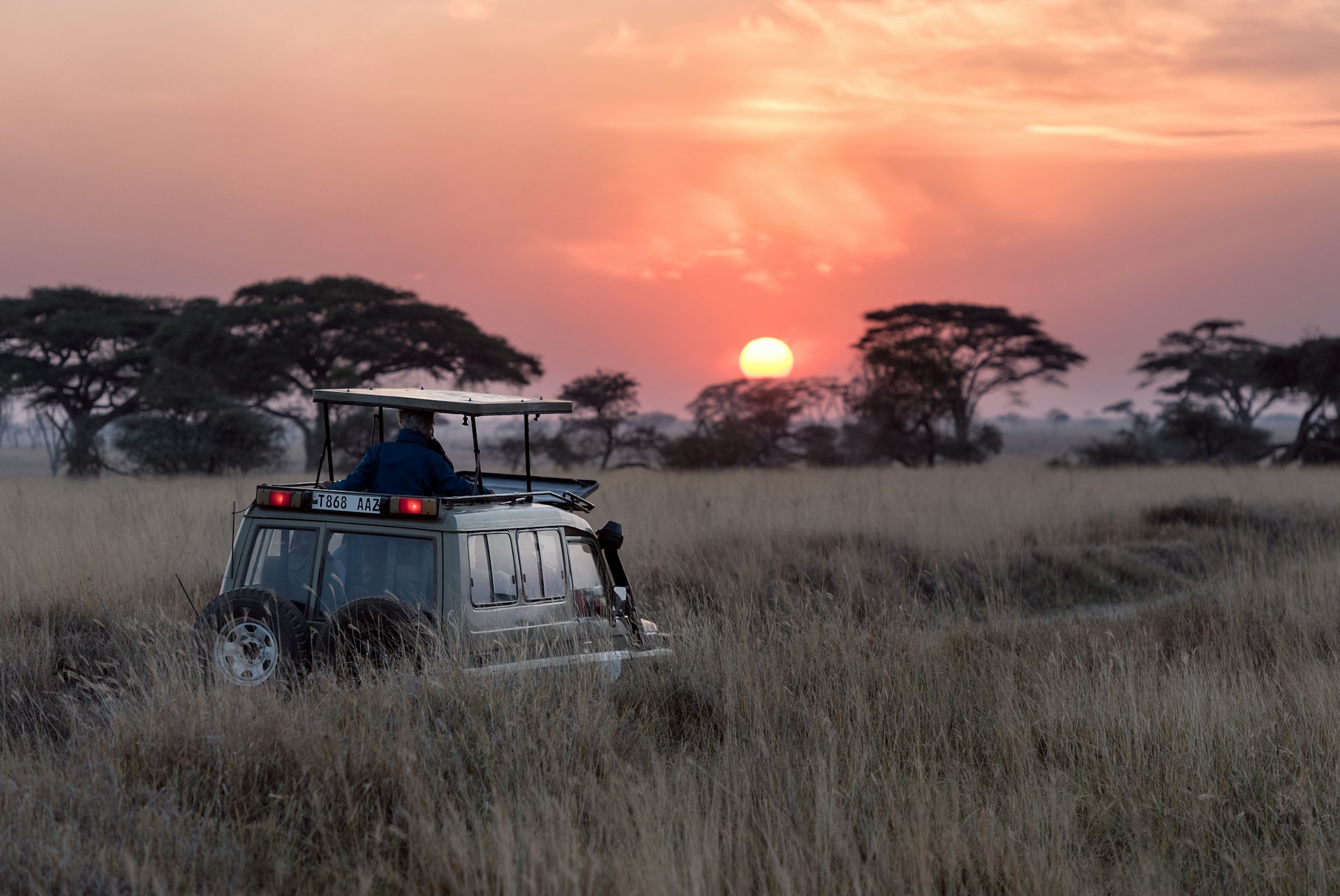 Serengeti, Tanzania - Tourists in a 4x4 car watching a breathtaking sunset over the savanna, capturing the essence of the Serengeti experience.