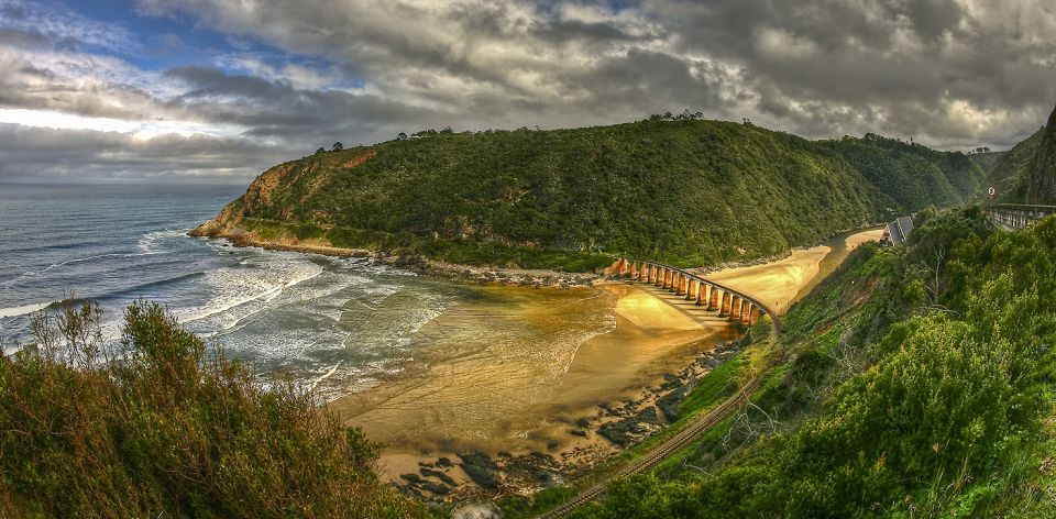 Scenic View of the Garden Route depicts some mountains surrounding a bay with a beach and the ocean.