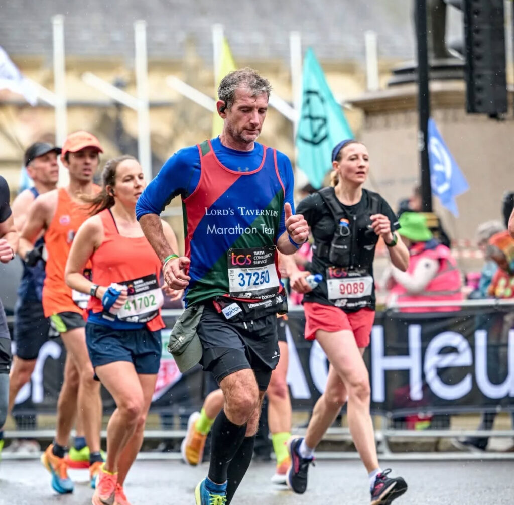 Our very own Christopher Bartlett running the London Marathon through the streets of London. Other racers in the background with the street audience behind the barriers.