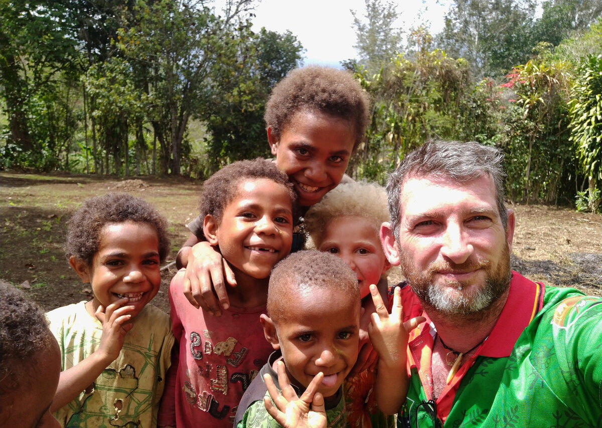 A perfect example About Us: Christopher Bartlett with some of the local children all holding each other huddled in for the picture. Big smiles on everyone's faces.