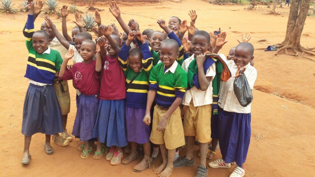 Happy Children standing together some of them rasing their hands all with big smiles on their faces.