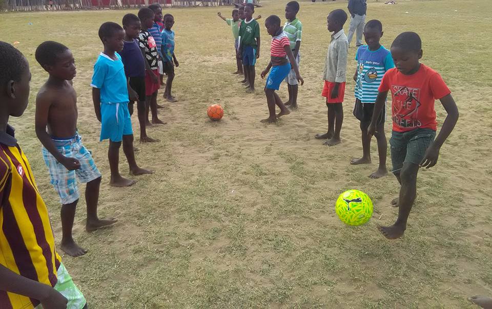 Children in a soccer team standing in 2 rows facing each other, training with a new soccer ball at the Ngame Soccer Academy, Zimbabwe.