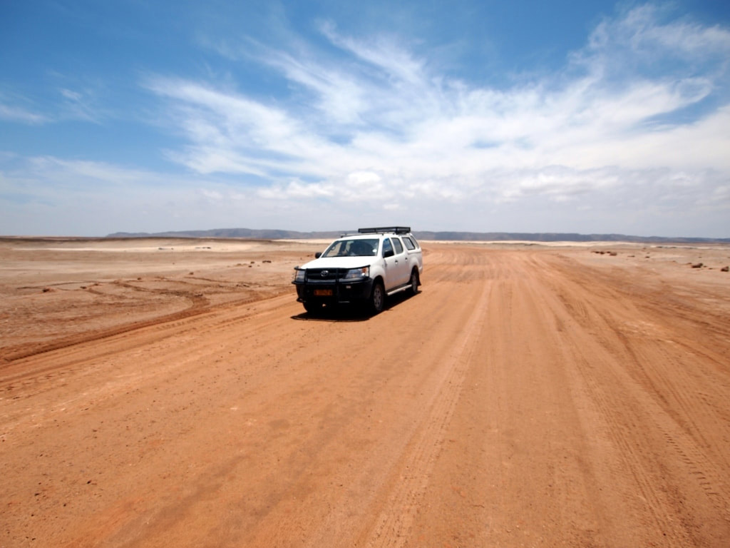 4 x 4 vehicle driving on a dirt road on the skeleton coast under blue skies.