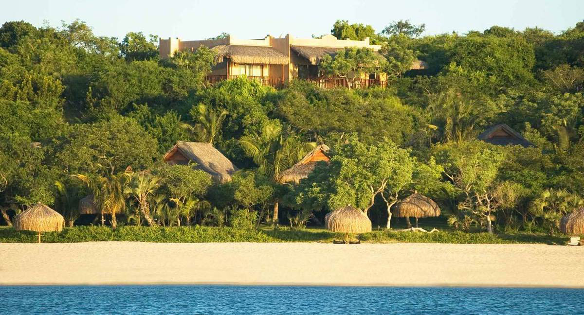 Picture fromt he ocean showing the beach and bay as well as accommodation in the tropical scene of pal trees.