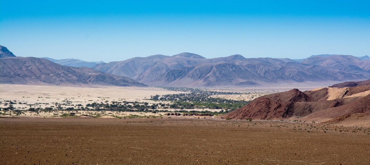 Beautiful Landscapes of Damaraland, mountains in the back ground and a small cluster of bushes in the middle ground.