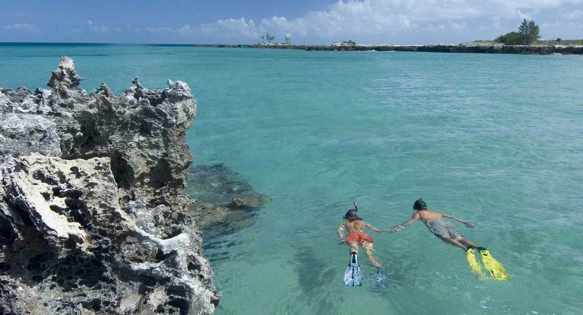 A honey Moon Couple taking a snorkel in turquoise clear water close to a rocky out crop in the calm waters.