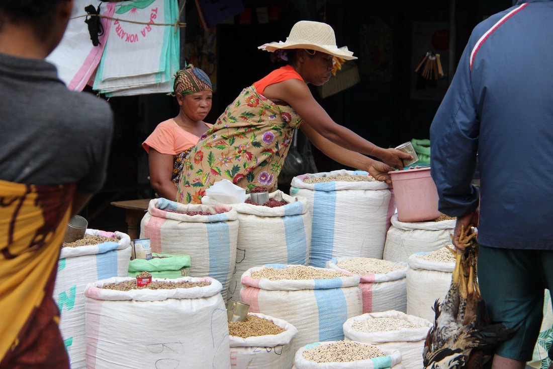 Busy seller in Madagascar's market, surrounded by bags of what looks like legumes and lentils that she sells.