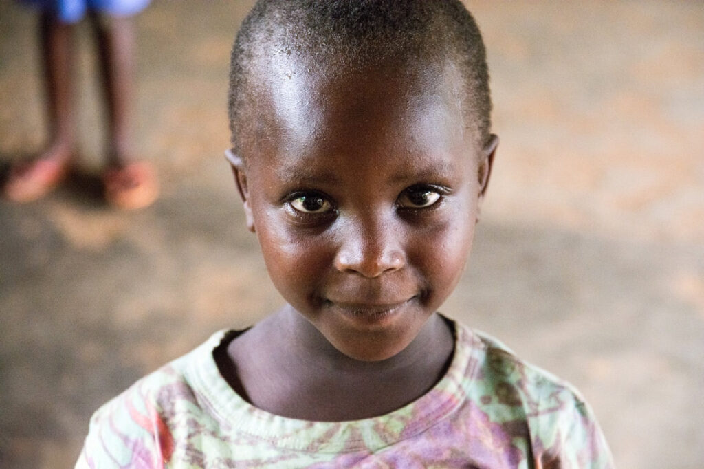A cute child that lives in Africa. Looking at the camera with a smile.