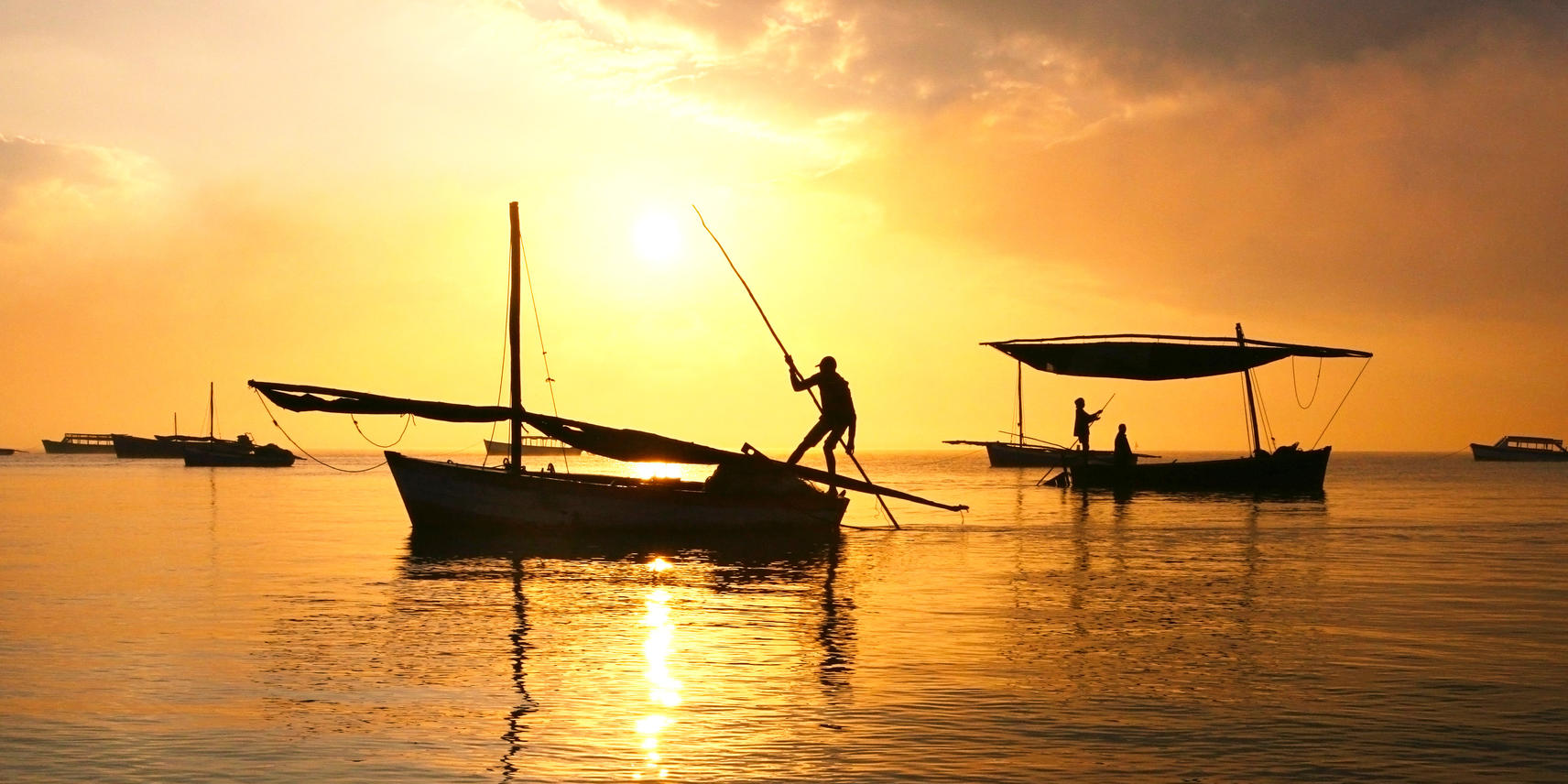 Dhows at sunset on the ocean and fisherman silhouetted by the golden reflection on the water