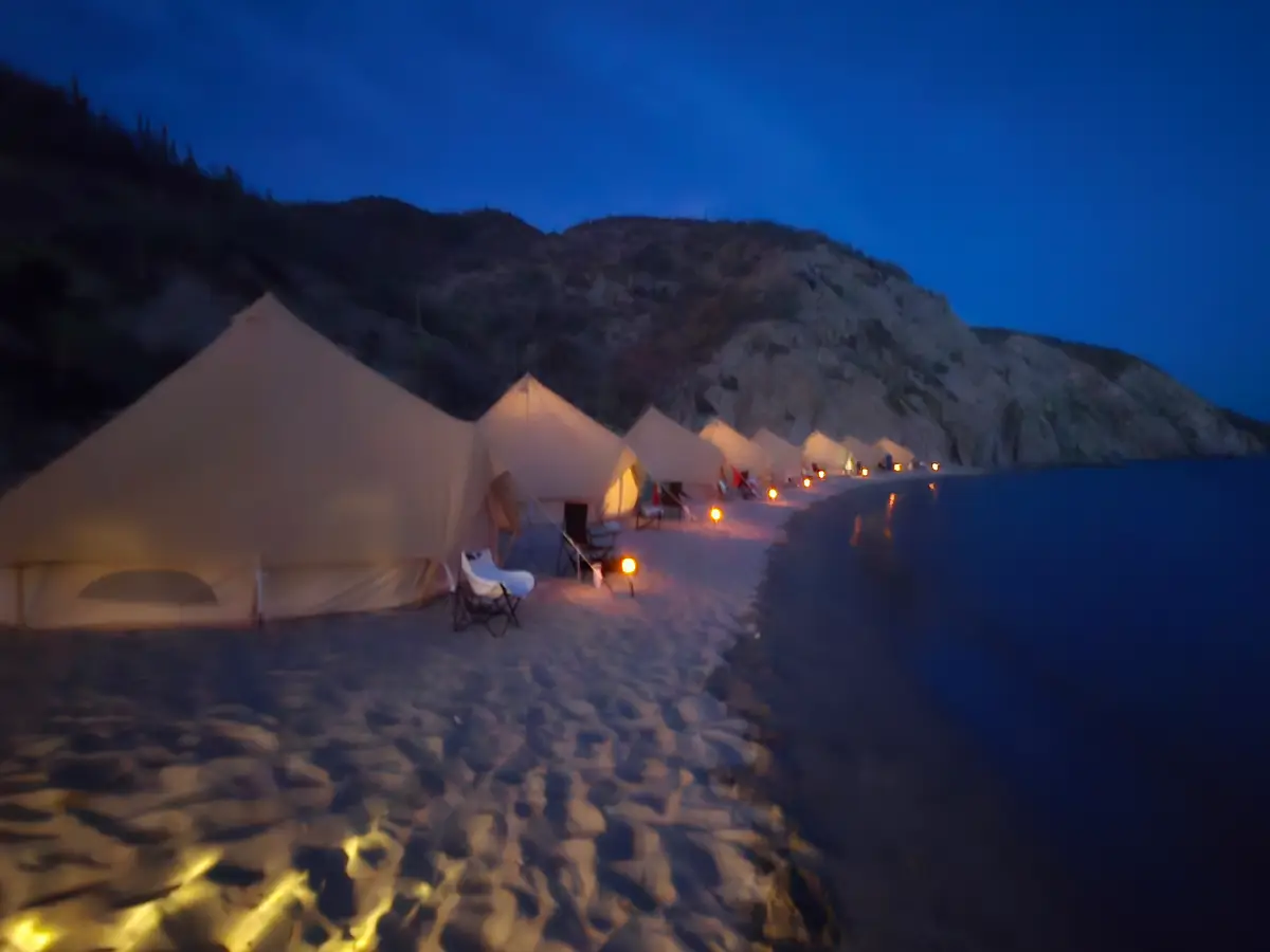 Night time image of the tents on the beach, lit up with a flat ocean and full moon light.